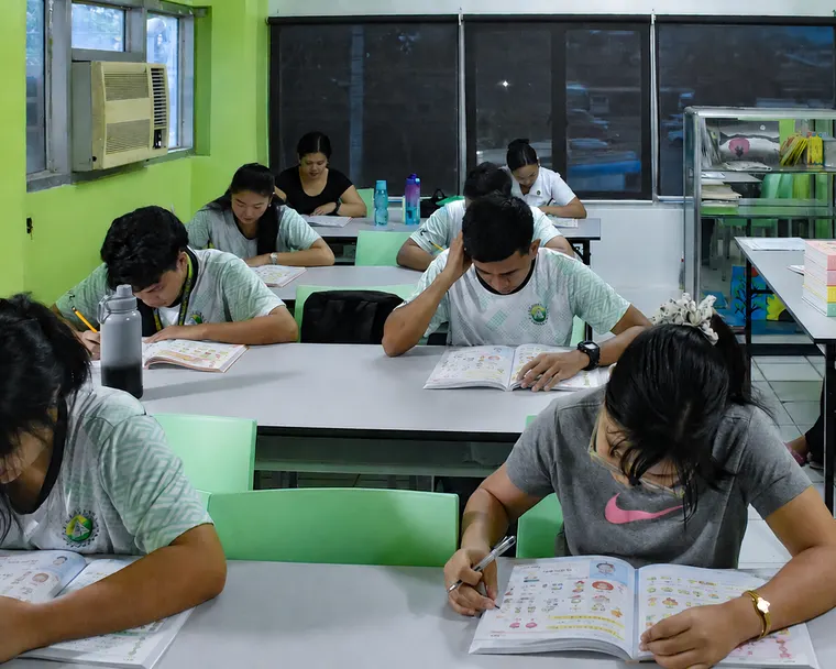 Students at classroom desks writing in Irodori workbooks, with stacked copies of the Irodori textbook series on a table nearby