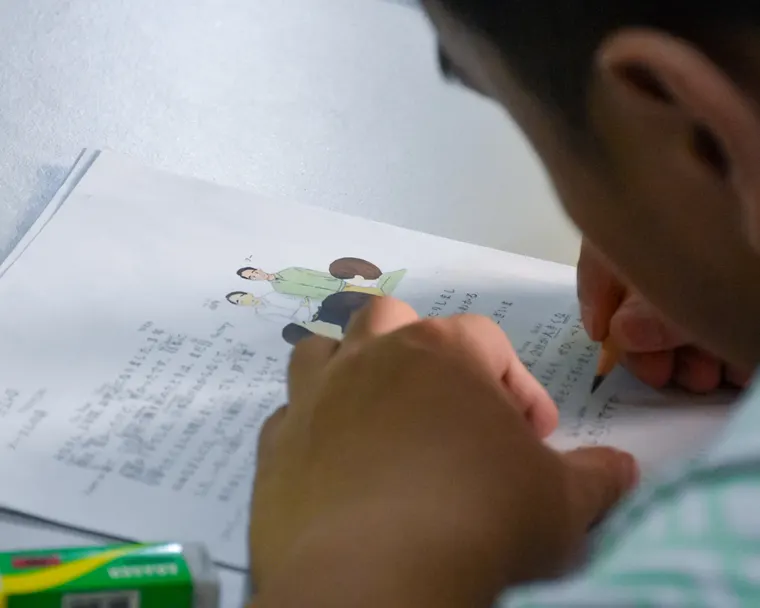 Close-up of a student's hand writing Japanese characters into a workbook during a review exercise