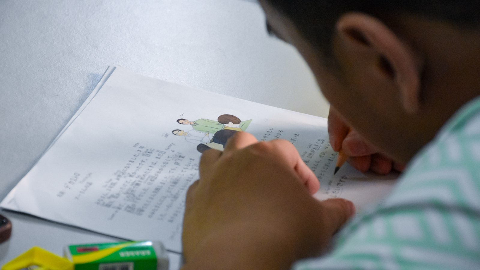 Close-up of a student writing Japanese characters into a review workbook