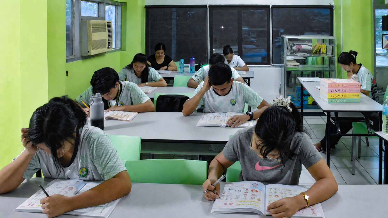 Students writing in Irodori workbooks at their desks, with stacked Irodori textbooks nearby